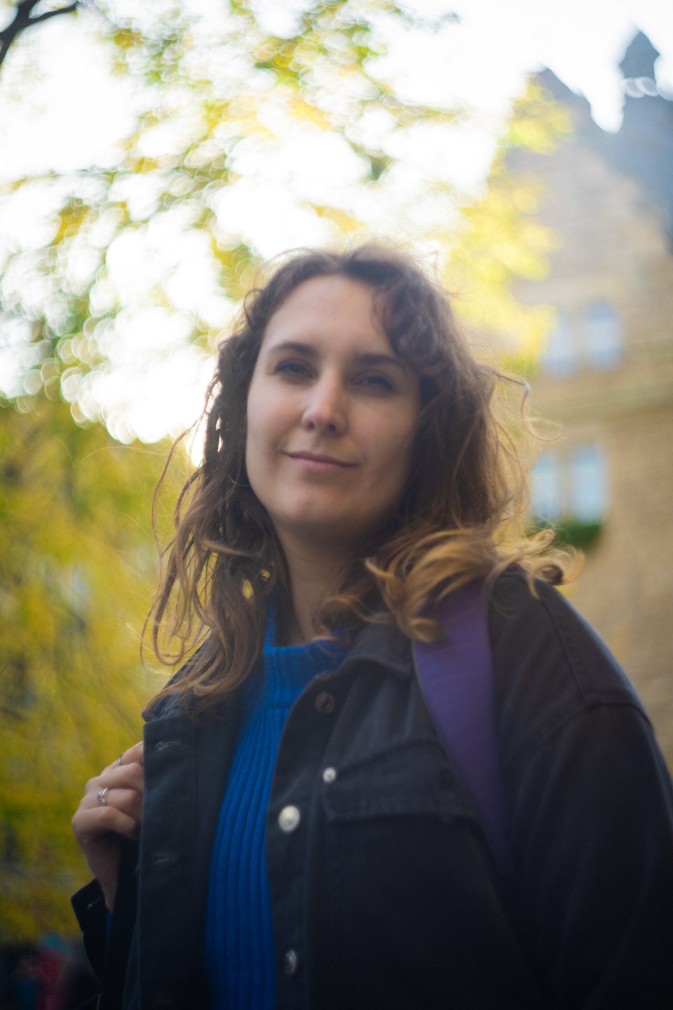 Sofía in a blue sweater and dark jacket, autumn trees behind her